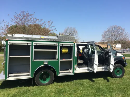 Exterior view of small fire truck showing cab, body compartments, and wheel/tire area.