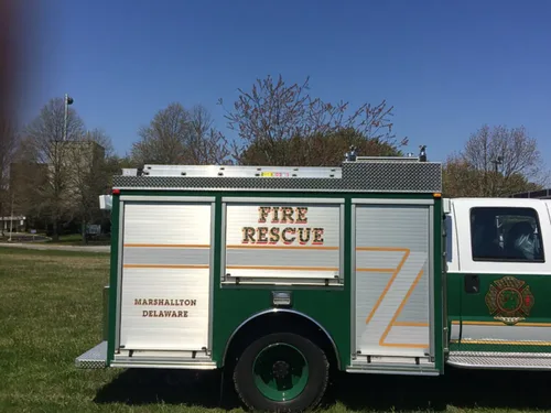 Exterior view of small fire truck showing cab, body compartments, and wheel/tire area.