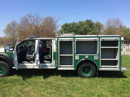 Exterior view of small fire truck showing cab, body compartments, and wheel/tire area.