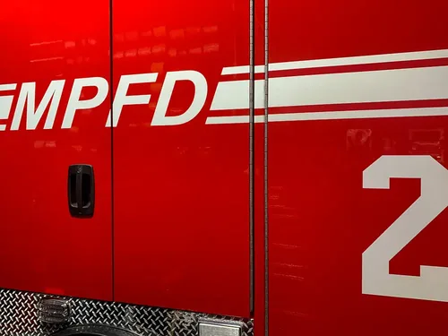 Exterior view of small fire truck showing cab, body compartments, and wheel/tire area.