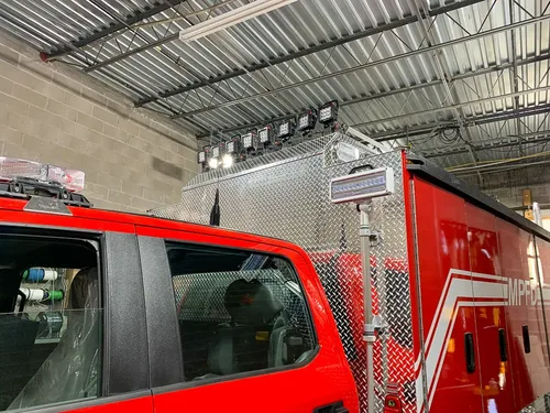 Exterior view of small fire truck showing cab, body compartments, and wheel/tire area.
