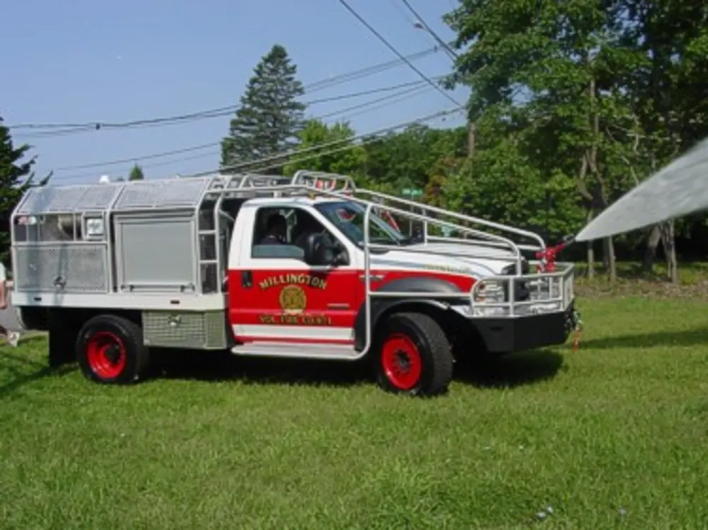 Exterior view of small fire truck showing cab, body compartments, and wheel/tire area.