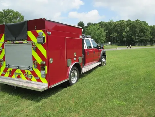 Exterior view of small fire truck showing cab, body compartments, and wheel/tire area.