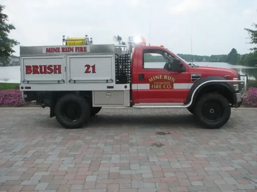 Exterior view of small fire truck showing cab, body compartments, and wheel/tire area.