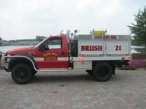 Exterior view of small fire truck showing cab, body compartments, and wheel/tire area.