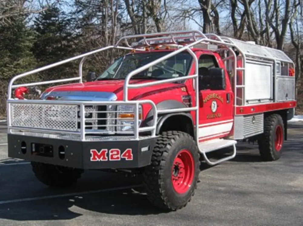 Exterior view of small fire truck showing cab, body compartments, and wheel/tire area.