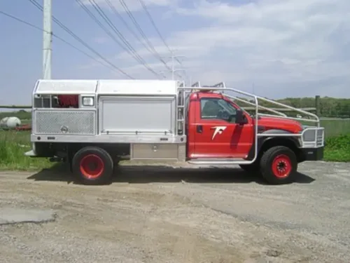 Exterior view of small fire truck showing cab, body compartments, and wheel/tire area.
