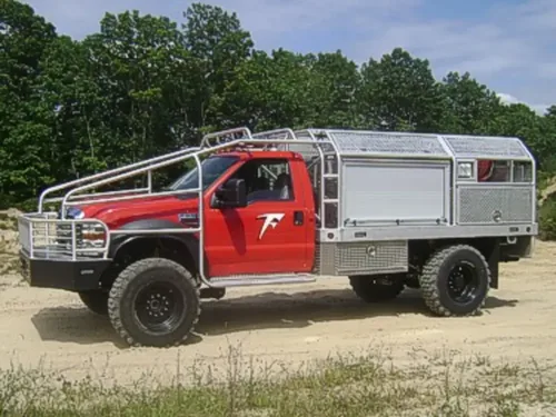 Exterior view of small fire truck showing cab, body compartments, and wheel/tire area.