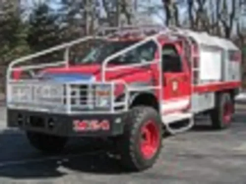 Exterior view of small fire truck showing cab, body compartments, and wheel/tire area.