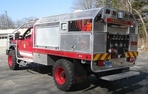 Exterior view of small fire truck showing cab, body compartments, and wheel/tire area.