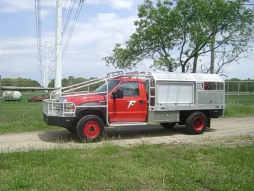 Exterior view of small fire truck showing cab, body compartments, and wheel/tire area.
