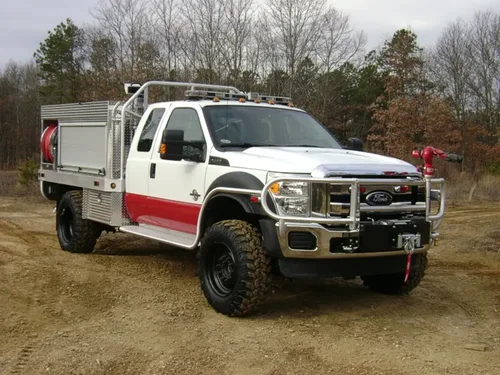 Exterior view of small fire truck showing cab, body compartments, and wheel/tire area.