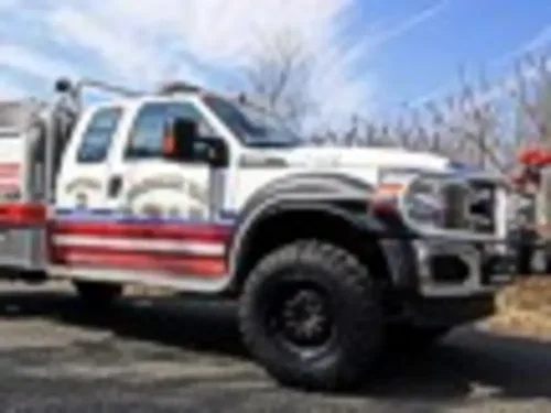 Exterior view of small fire truck showing cab, body compartments, and wheel/tire area.