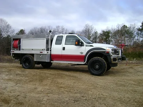 Exterior view of small fire truck showing cab, body compartments, and wheel/tire area.