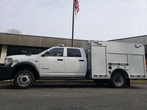 Exterior view of small fire truck showing cab, body compartments, and wheel/tire area.