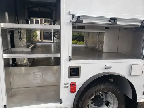 Exterior view of small fire truck showing cab, body compartments, and wheel/tire area.