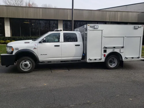 Exterior view of small fire truck showing cab, body compartments, and wheel/tire area.