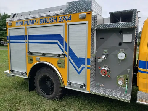 Exterior view of small fire truck showing cab, body compartments, and wheel/tire area.