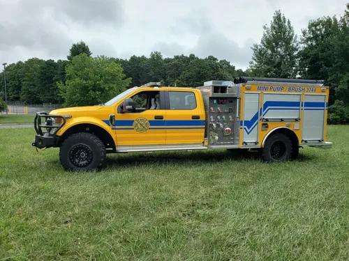 Exterior view of small fire truck showing cab, body compartments, and wheel/tire area.