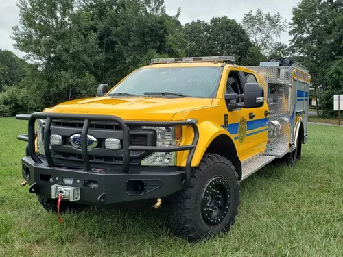 Exterior view of small fire truck showing cab, body compartments, and wheel/tire area.