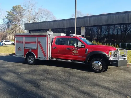 Exterior view of small fire truck showing cab, body compartments, and wheel/tire area.