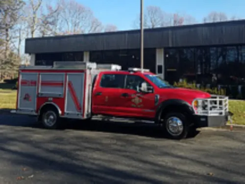 Exterior view of small fire truck showing cab, body compartments, and wheel/tire area.