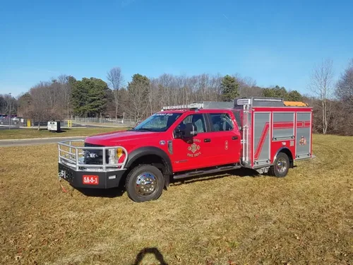 Exterior view of small fire truck showing cab, body compartments, and wheel/tire area.