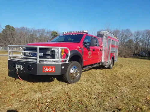 Exterior view of small fire truck showing cab, body compartments, and wheel/tire area.