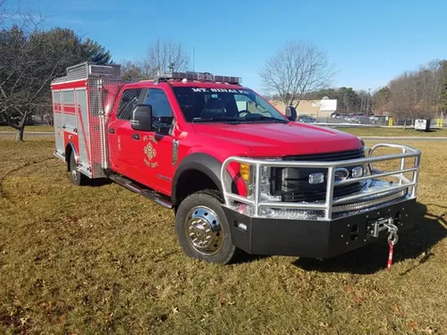 Exterior view of small fire truck showing cab, body compartments, and wheel/tire area.