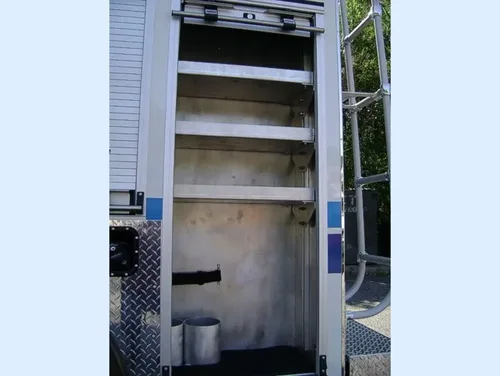 Exterior view of small fire truck showing cab, body compartments, and wheel/tire area.