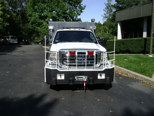 Exterior view of small fire truck showing cab, body compartments, and wheel/tire area.