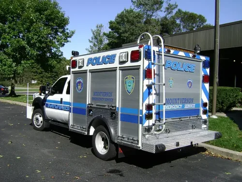 Exterior view of small fire truck showing cab, body compartments, and wheel/tire area.
