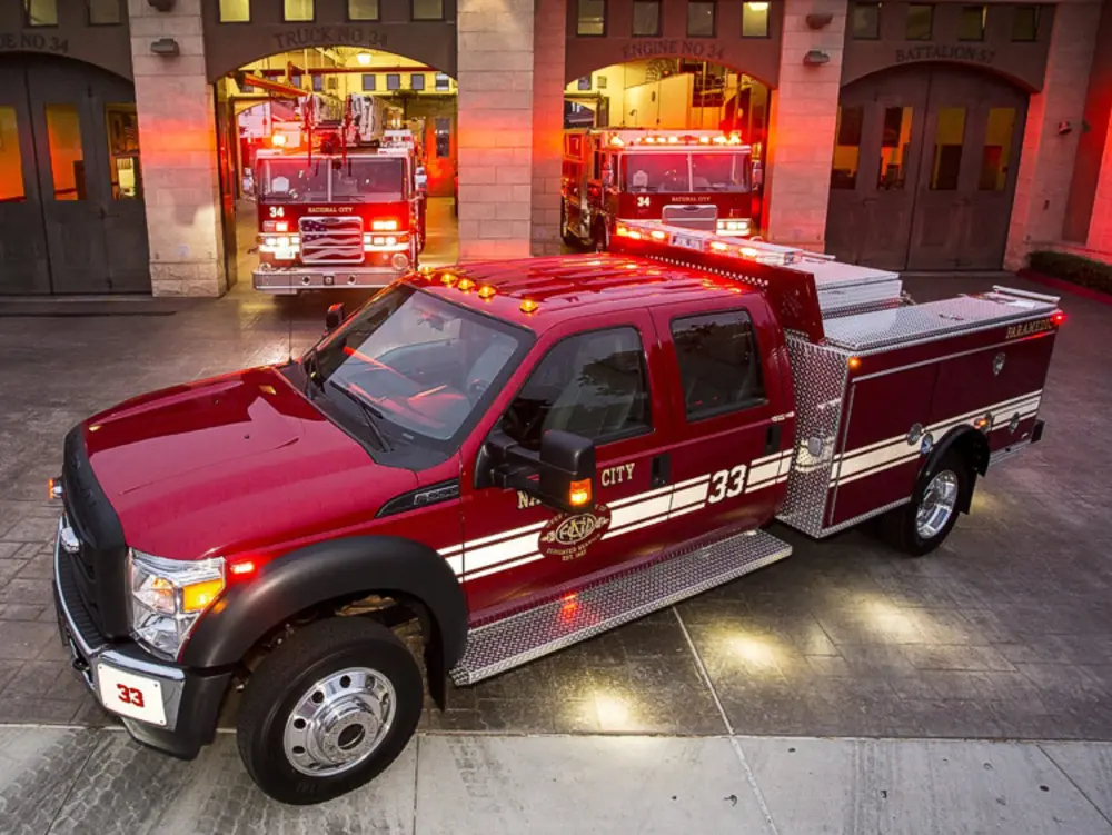 Exterior view of small fire truck showing cab, body compartments, and wheel/tire area.
