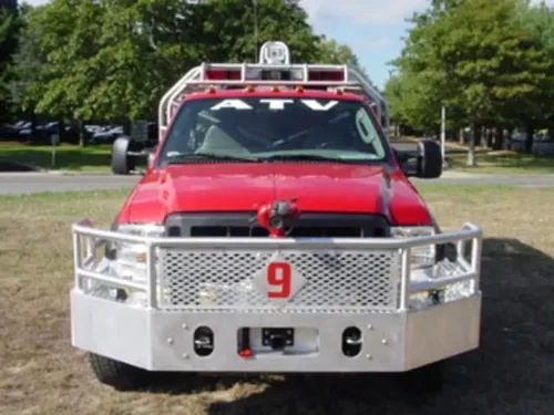 Exterior view of small fire truck showing cab, body compartments, and wheel/tire area.