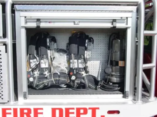 Exterior view of small fire truck showing cab, body compartments, and wheel/tire area.