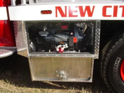 Exterior view of small fire truck showing cab, body compartments, and wheel/tire area.