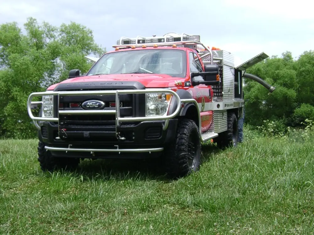 Exterior view of small fire truck showing cab, body compartments, and wheel/tire area.