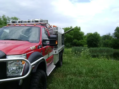 Exterior view of small fire truck showing cab, body compartments, and wheel/tire area.