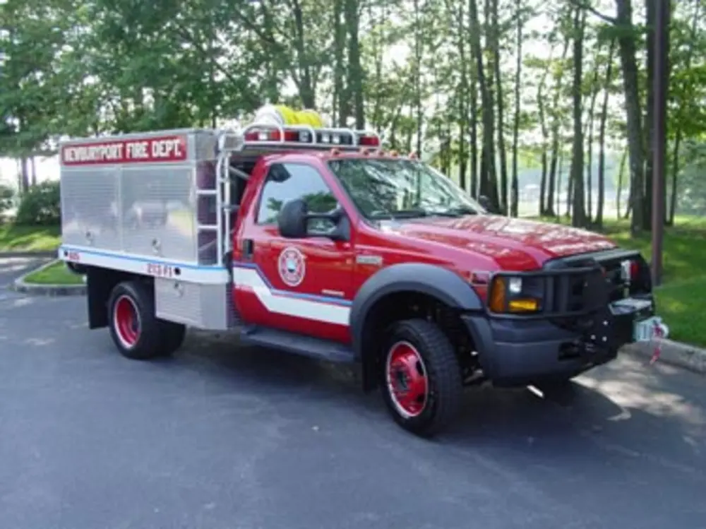 Exterior view of small fire truck showing cab, body compartments, and wheel/tire area.