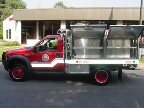 Exterior view of small fire truck showing cab, body compartments, and wheel/tire area.