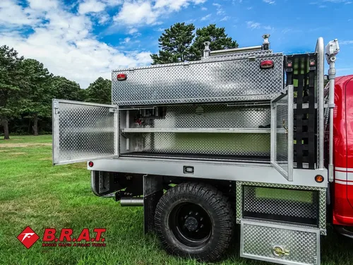 Exterior view of small fire truck showing cab, body compartments, and wheel/tire area.