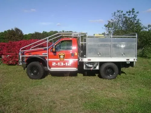 Exterior view of small fire truck showing cab, body compartments, and wheel/tire area.