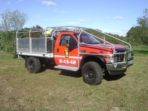 Exterior view of small fire truck showing cab, body compartments, and wheel/tire area.