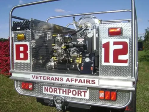 Exterior view of small fire truck showing cab, body compartments, and wheel/tire area.
