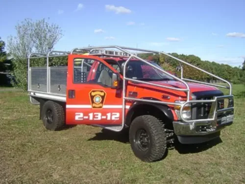 Exterior view of small fire truck showing cab, body compartments, and wheel/tire area.