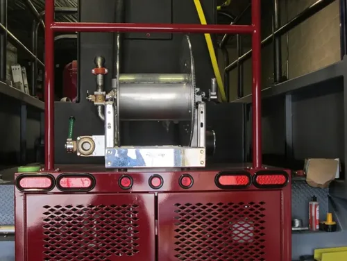 Exterior view of small fire truck showing cab, body compartments, and wheel/tire area.