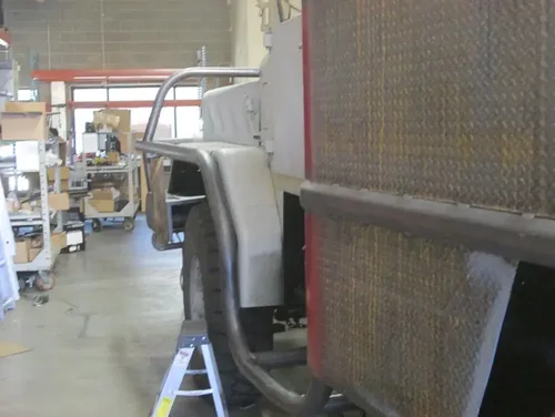 Exterior view of small fire truck showing cab, body compartments, and wheel/tire area.