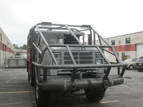 Exterior view of small fire truck showing cab, body compartments, and wheel/tire area.