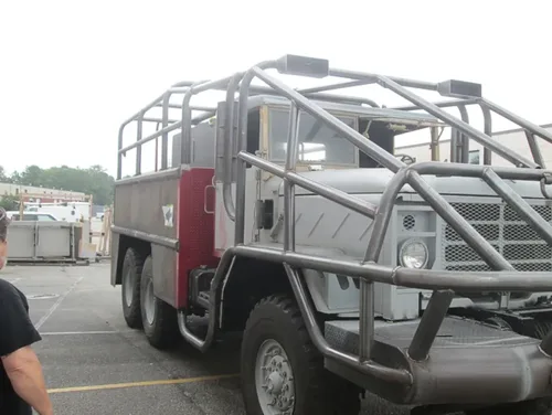 Exterior view of small fire truck showing cab, body compartments, and wheel/tire area.