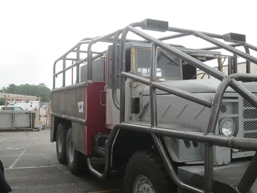 Exterior view of small fire truck showing cab, body compartments, and wheel/tire area.